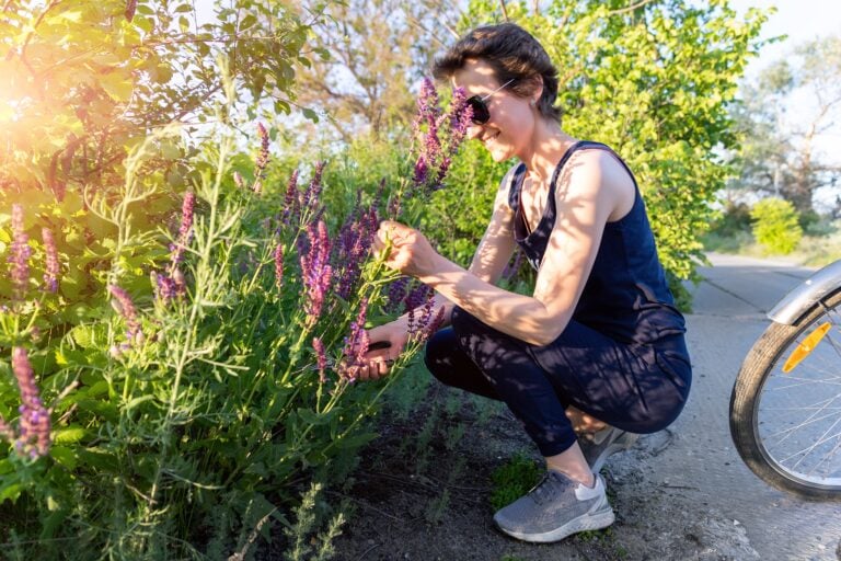 Portrait of young adult happy caucasian woman gathering sage herbs wild flowers bouquet at meadow outdoors