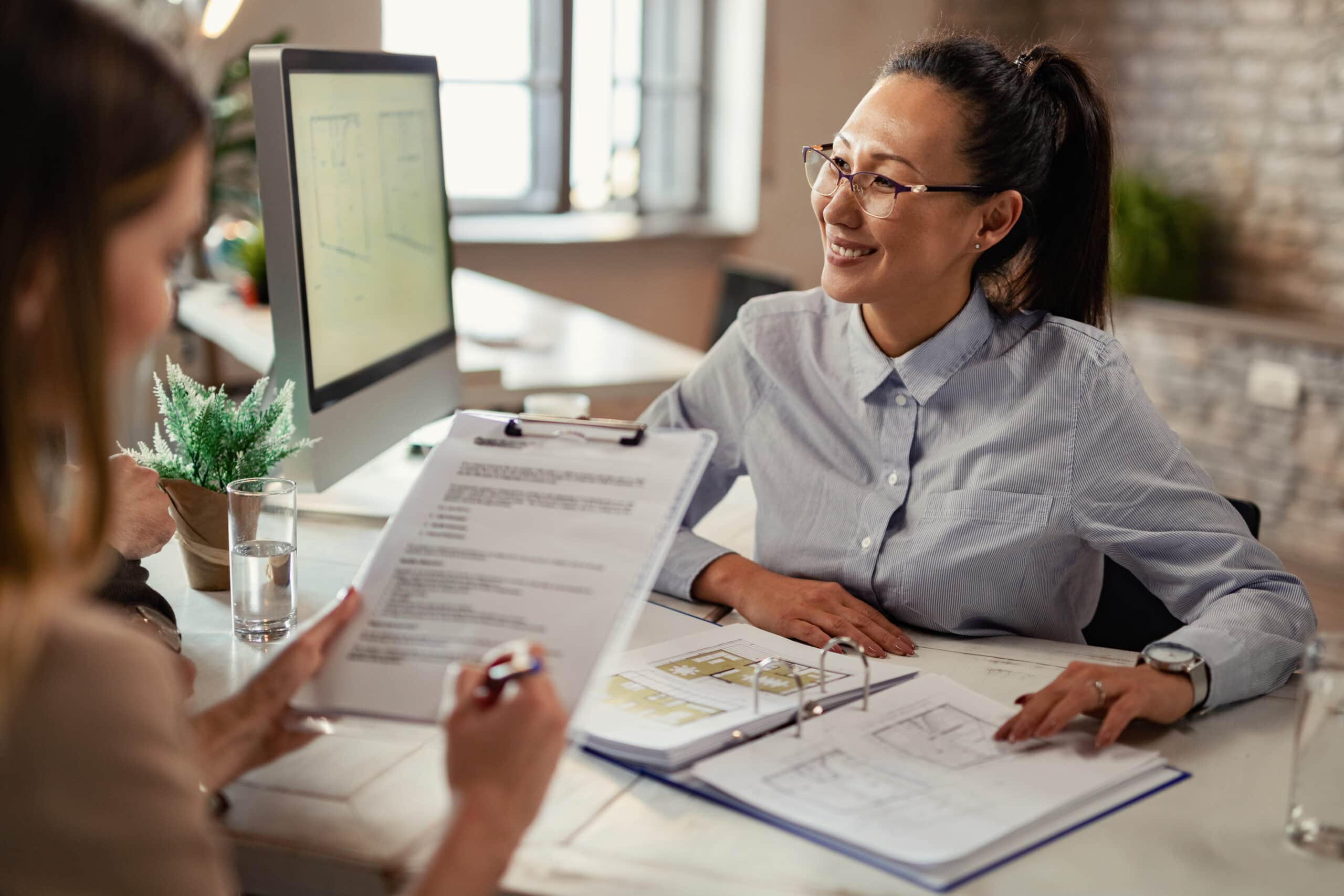 Happy Asian insurance agent communicating with her clients during a meeting in the office.