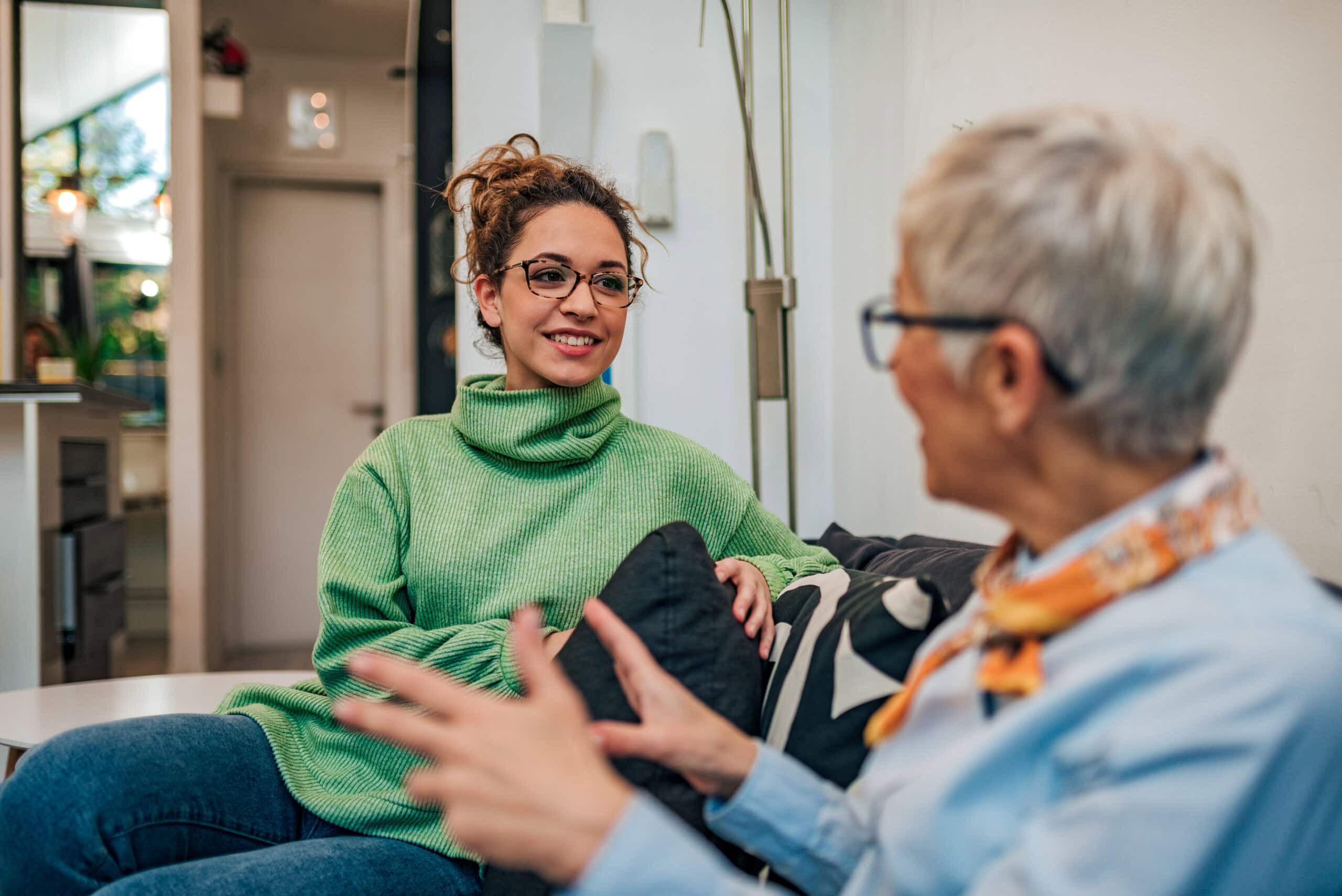 Smiling young woman talking and listening to her grandmother, at home.